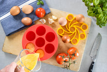 Load image into Gallery viewer, Red silicone mould and yellow trivet on a cutting board with eggs, tomatoes, and garlic