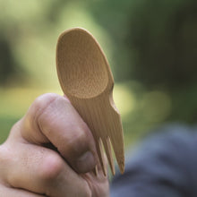 Load image into Gallery viewer, A hand holding a single-piece bamboo spork with a blurred natural background.