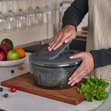 Load image into Gallery viewer, Person using a salad spinner on a kitchen counter with fruits and vegetables around