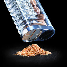 Load image into Gallery viewer, Clear cylindrical container with a metal blade grinding brown powdered nutmeg onto a black background