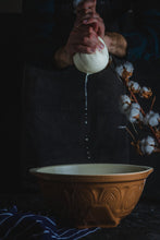 Load image into Gallery viewer, Person squeezing a whey from a muslin cloth with homemade cheese into an orange bowl with cotton plants in the background