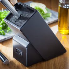 Load image into Gallery viewer, Black knife block on a wooden surface with vegetables and a bottle in the background.
