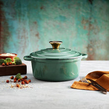 Load image into Gallery viewer, A green cast iron casserole dish with lid and two handles on a kitchen counter.