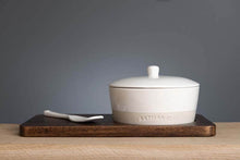 Load image into Gallery viewer, A white ceramic cheese baker set with a lid and a wooden server, placed on a dark acacia wood tray.