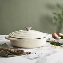 Load image into Gallery viewer, A green cast iron casserole dish with lid and two handles on a kitchen counter.