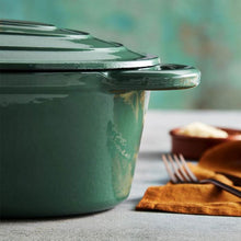 Load image into Gallery viewer, A green cast iron casserole dish with lid and two handles on a kitchen counter.