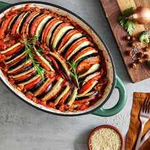 Load image into Gallery viewer, A green cast iron casserole dish with lid and two handles on a kitchen counter. Containing food. Ratatouille.