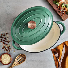 Load image into Gallery viewer, A green cast iron casserole dish with lid and two handles on a kitchen counter.