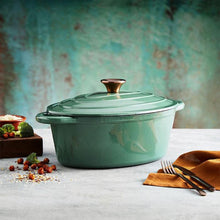 Load image into Gallery viewer, A green cast iron casserole dish with lid and two handles on a kitchen counter.