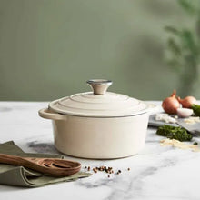 Load image into Gallery viewer, A green cast iron casserole dish with lid and two handles on a kitchen counter.