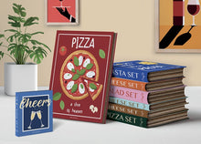Load image into Gallery viewer, Stack of books with food-themed covers on a table with decorative elements.
