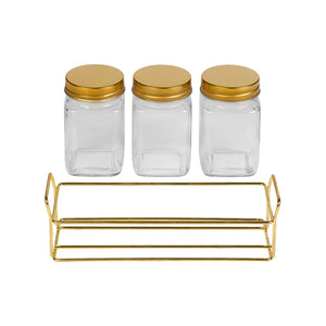 Three glass jars with gold lids and a gold metal shelf on a white background