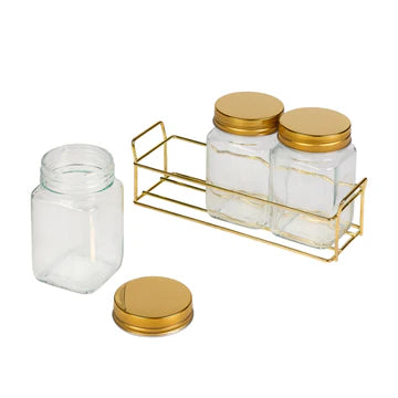 Set of glass jars with gold lids and a gold metal organizer on a white background