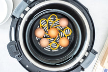 Load image into Gallery viewer, Eggs inside an air fryer with a patterned trivet underneath.
