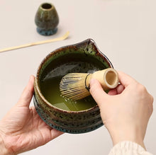 Load image into Gallery viewer, hand holding bamboo matcha tea whisk being used in caramic bowl on white background
