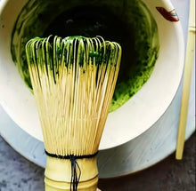 Load image into Gallery viewer, bamboo matcha tea whisk with green tea in background
